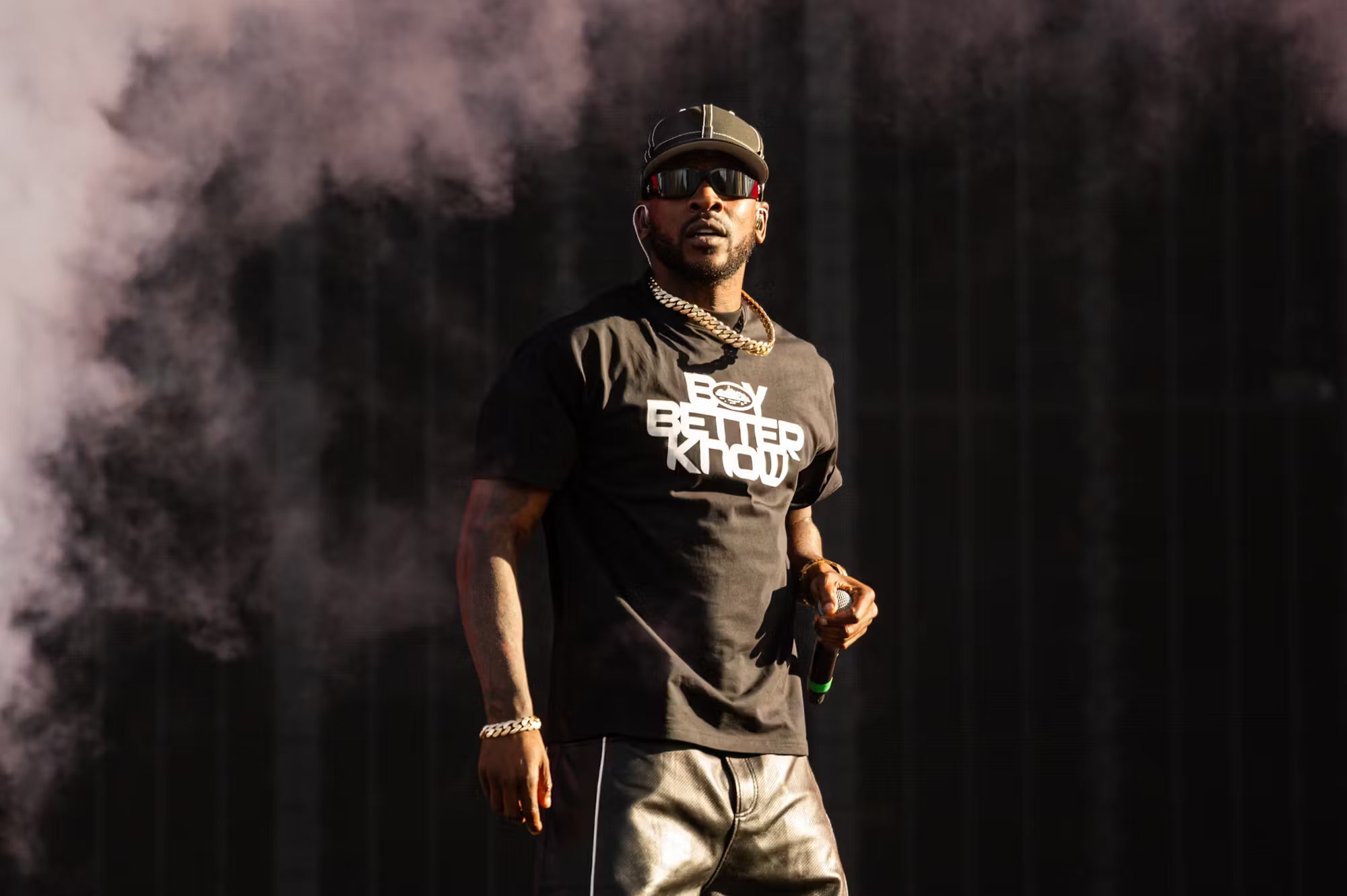 Person wearing a black t-shirt with text, standing against a dark background with smoke.
